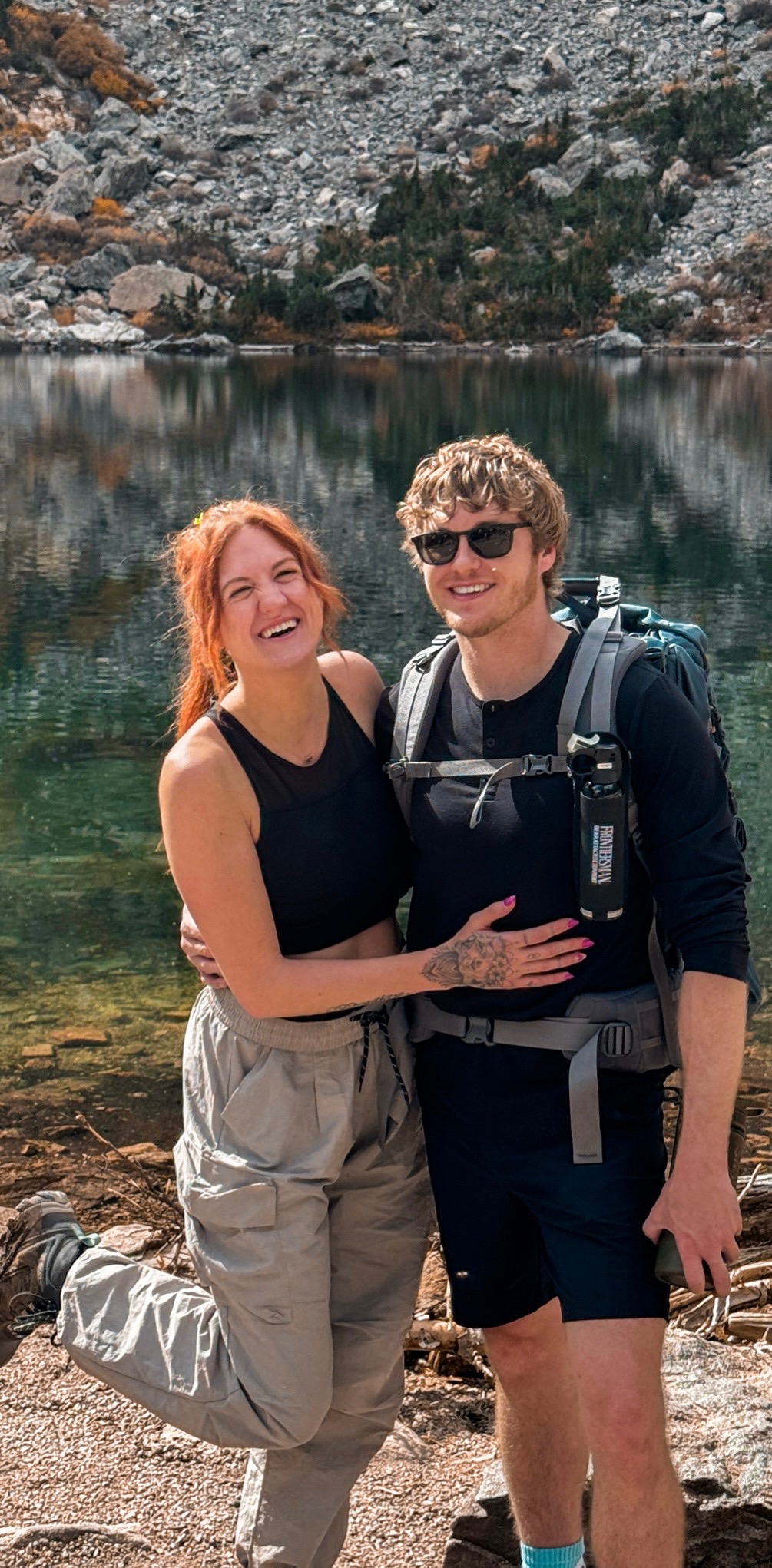 Jake and Em smiling together beside a mountain lake